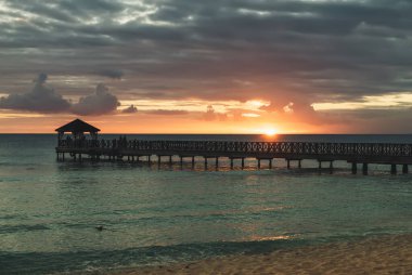 Dominik Cumhuriyeti 'ndeki güzel Karayip plajı. Mavi deniz suyu, renkli gökyüzü ve ahşap iskele ile tropikal cennet manzarası.
