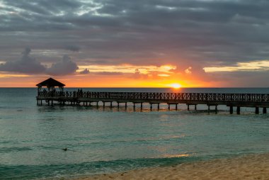 Dominik Cumhuriyeti 'ndeki güzel Karayip plajı. Mavi deniz suyu, renkli gökyüzü ve ahşap iskele ile tropikal cennet manzarası.