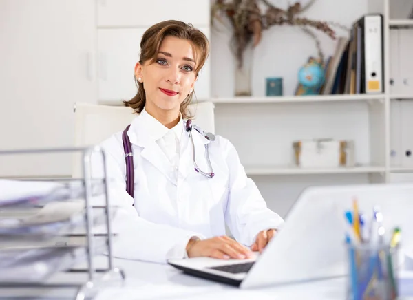 Portret Pozytywnej Lekarki Siedzącej Przy Stole Roboczym Biurze Korzystającej Laptopa — Zdjęcie stockowe