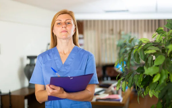 クリップボードでオフィスに立つ朗らかな笑顔の看護師の女性 医学史シートを書く — ストック写真
