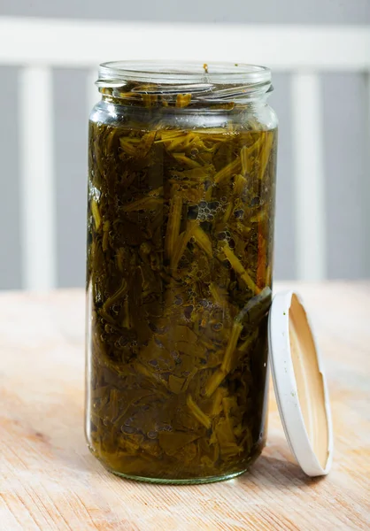 木製の表面に開いたガラス瓶の中に缶詰の緑のほうれん草 — ストック写真