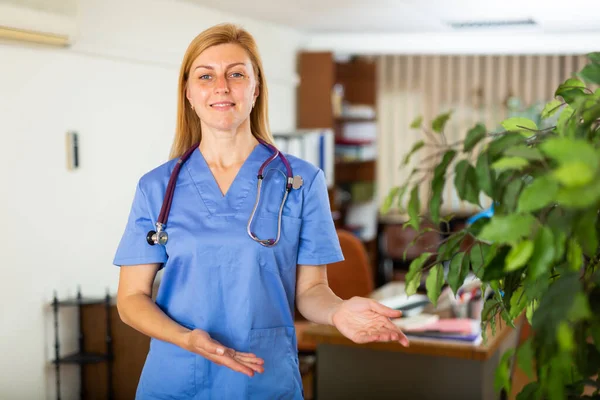 医療事務所に立つ正のヨーロッパの女性医師アシスタントは歓迎ジェスチャーを作ります — ストック写真