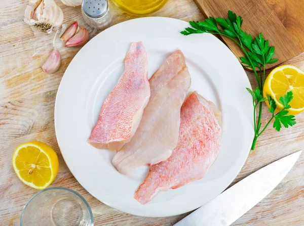 stock image Raw rockfish fillet on plate, garlic, parsley and salt on wooden table. Ingredients for cooking