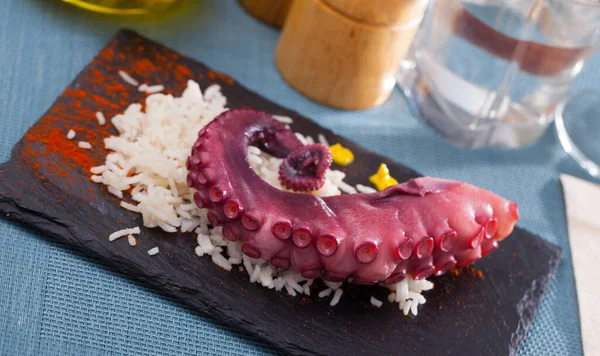 Boiled octopus with rice served on slate with paprika and sauce