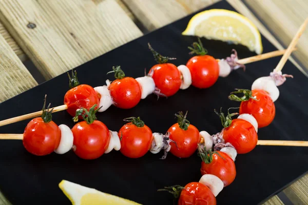 Grilled mini-squid with cherry tomatoes with olive oil and balsamic served on wood skewers with lemon