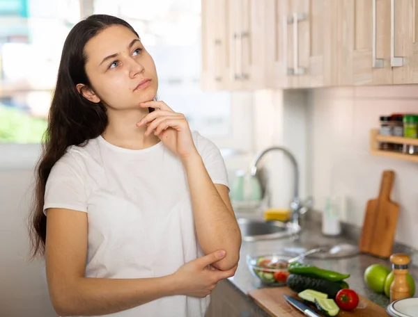 Confused young woman standing at kitchen, having problems in cooking