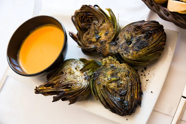 stock image Traditional Catalan vegetarian appetizer of chargrilled artichokes on white plate with piquant romesco..