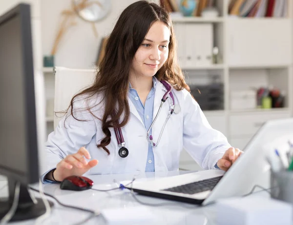診療所でノートパソコンや書類を扱う女性医師の肖像画 — ストック写真