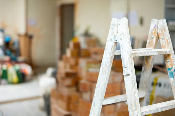 屋内建築現場で塗料や石膏の汚れを持つはしご 背景に積層様々な建築材料 — ストック写真