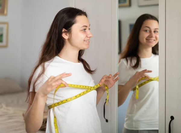 快乐的年轻漂亮女人在家里用测量带测量乳房 — 图库照片