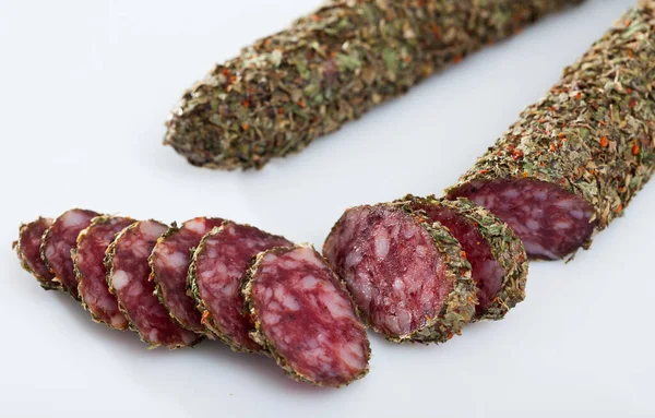 Image of spanish fuet with herbs sausages cut in slices on a white surface, close-up