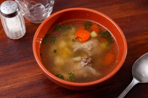 Appetizing light soup cooked in meat broth from potatoes, carrots, greenery with pork slices
