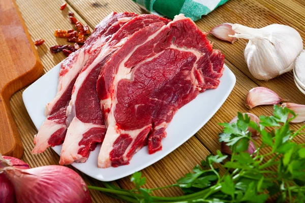 木のテーブルの上にパセリとニンニクと調理されていない牛肉の切り身 — ストック写真