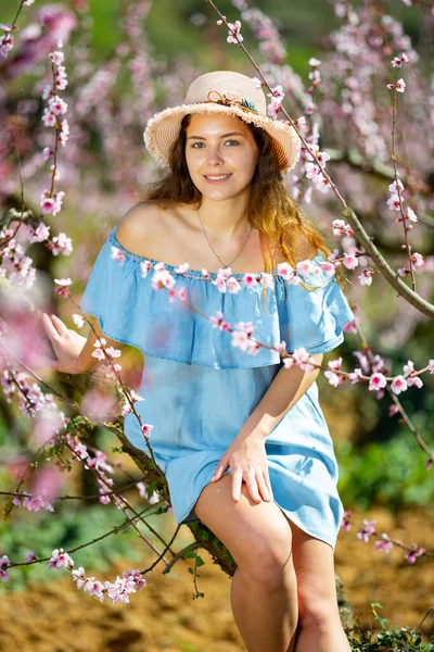Atrakcyjna Amerykańska Kobieta Słomkowym Kapeluszu Pozująca Pod Brzoskwinią Kwitnącym Wiosennym — Zdjęcie stockowe