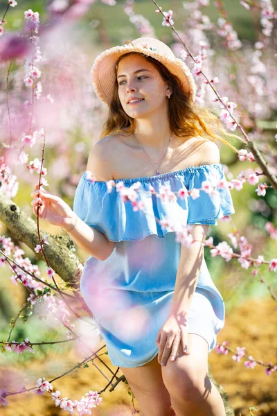春天里 戴着草帽的年轻漂亮的女人在美丽的公园里欣赏大自然 桃树盛开 — 图库照片