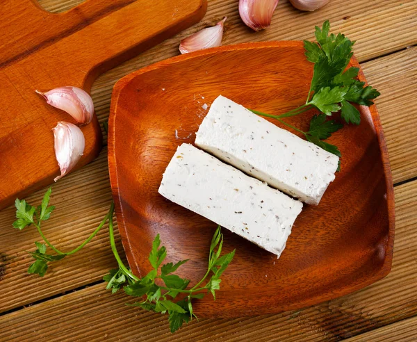 Log-shaped fresh goat-milk cheese with herbs on plate on wooden surface