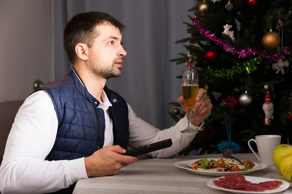 Man having christmas dinner with champagne and watching tv at home.