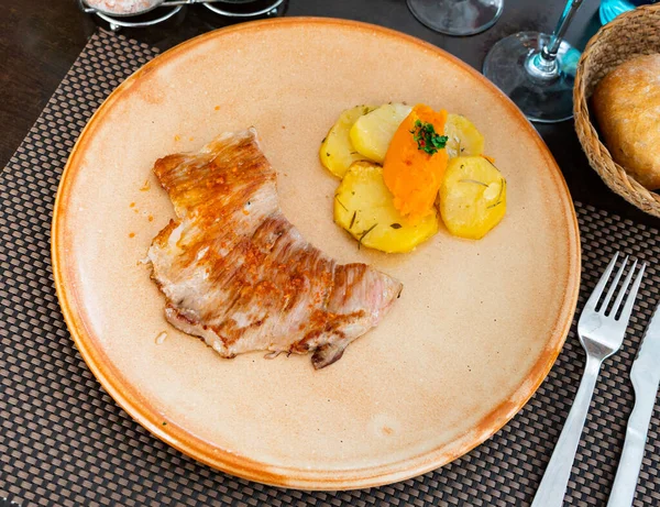 Traditional Spanish dish, secreto, served on plate with potato slices and sweet potato puree on plate in restaurant.