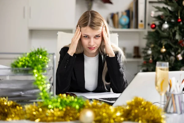 Sad woman employee working in office with documents and laptop during Christmas time