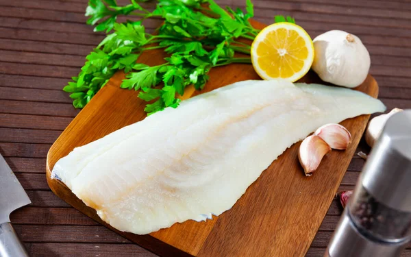 Image of fillet of raw cod fillet before cooking on wooden background with garlic and greens
