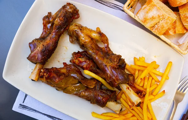Appetizing spicy baked lamb shins served with vegetable garnish of french fries