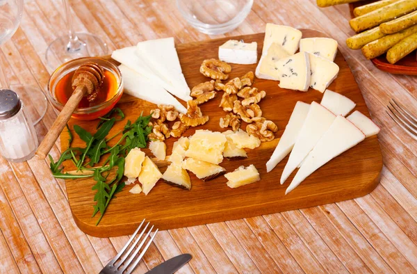 チーズボードには蜂蜜とクルミが添えられ 木製のテーブルの上にハーブが飾られています — ストック写真