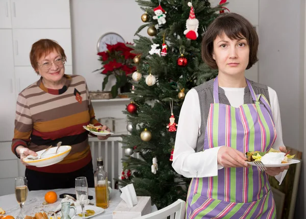 大人の娘は 彼女の母親が家族のクリスマスのお祝いの後にテーブルから料理をクリアするのを助ける — ストック写真