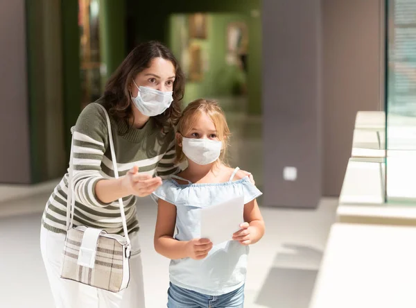 艺术博物馆里戴着口罩带着女儿的妇女 指着艺术品 — 图库照片
