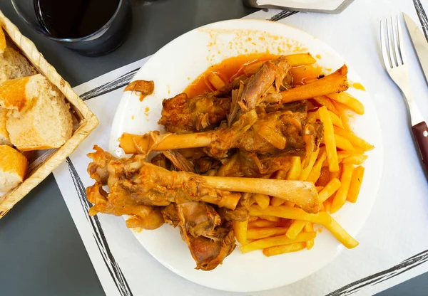 Appetizing baked lamb shins from oven with sauce served with vegetable garnish of french fries