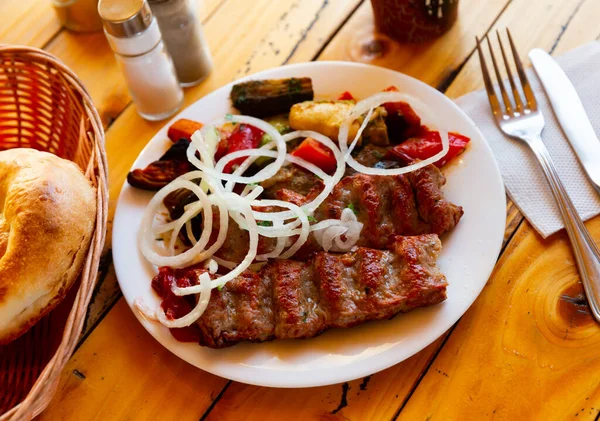 东方料理中受欢迎的肉食是带有烤蔬菜的腊肠烤羊肉 顶部装饰有切碎的洋葱圈 — 图库照片