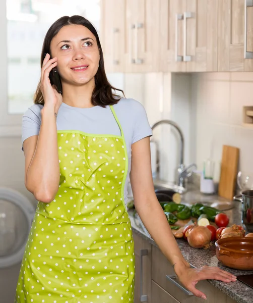 穿着围裙的年轻女家庭主妇在家里厨房打电话聊天的画像 — 图库照片