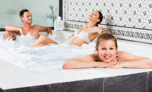 快乐积极的三位朋友在温泉浴场享受按摩浴缸泡泡浴 — 图库照片