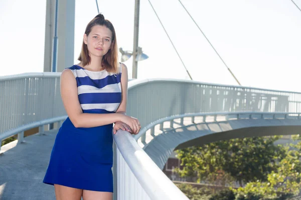 穿着蓝色衣服站在现代城市桥上的年轻而积极的女孩 — 图库照片