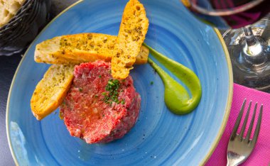 Picture of raw veal steak tartar served at blue plate with fried toasts on cafe clipart