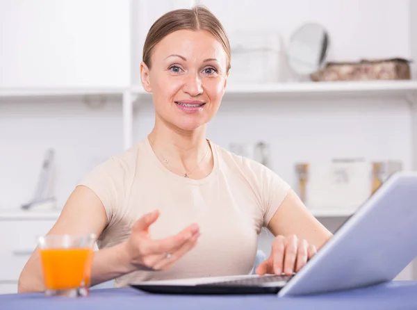 笑顔の女性はテーブルに座って 自宅でノートパソコンで作業 — ストック写真