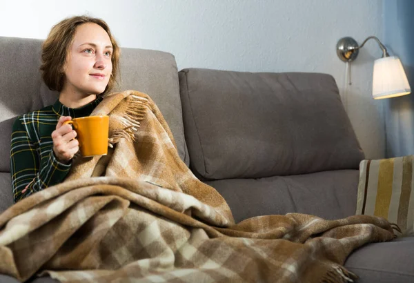微笑的女孩坐在客厅的沙发上喝茶 — 图库照片
