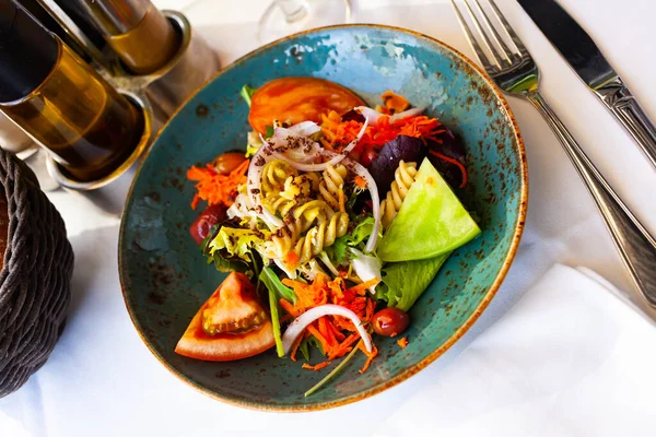 白いテーブルの上に青いセラミックプレートでパスタや新鮮な野菜とおいしいサラダ — ストック写真
