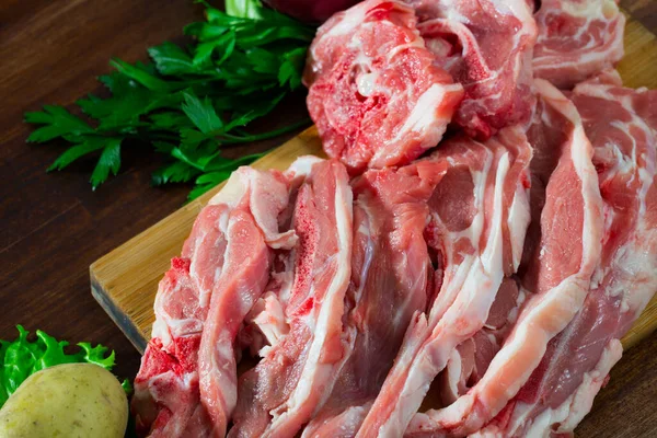 新鮮な野菜や緑を背景に木製のまな板上の生ラム肉肉 — ストック写真