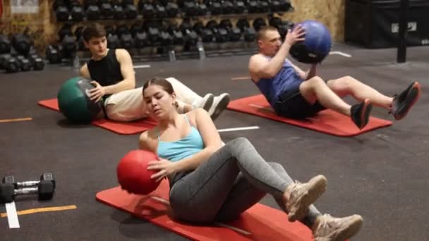 スポーツの若い女の子はジムでのグループトレーニング中に腹筋の筋肉を強化するために薬ボールとのねじれ座位を行う アクティブライフスタイルのコンセプト 高品質4K映像 — ストック動画