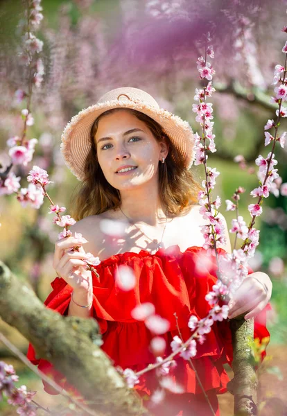 若いです幸せな女性で藁帽子でポーズ春の公園で咲く木を背景に — ストック写真
