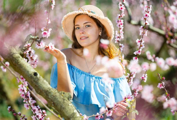 드레스를 아가씨와 배경에 꽃피는 나무가 공원에 포즈를 취하고 모자를 — 스톡 사진