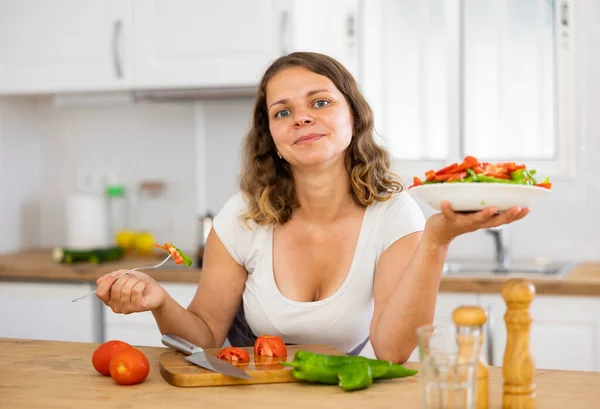 キッチンで新鮮な野菜サラダを楽しむ笑顔の若い女性の肖像画 — ストック写真