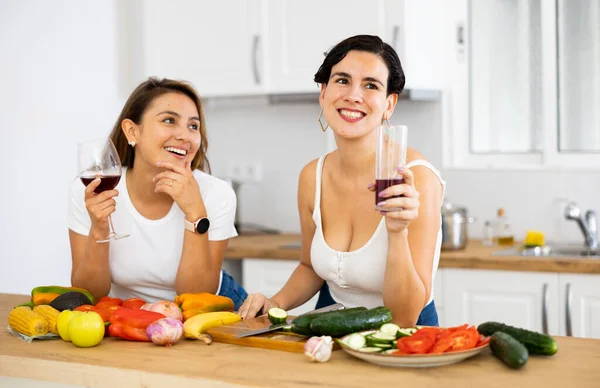 野菜のサラダを準備しながら 家庭のキッチンで妹と一緒に若いヒスパニック系の女性料理を笑って 陽気にチャットやワインを飲みます 幸せな家族関係の概念 — ストック写真