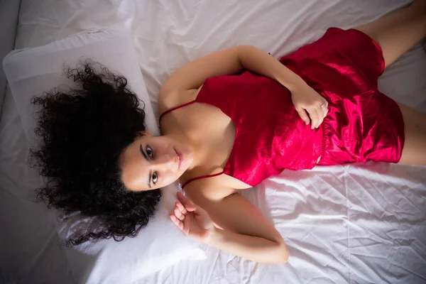 Kırmızı Ipek Pijamalı Gülümseyen Genç Bir Kadın Evdeki Beyaz Yatağa — Stok fotoğraf
