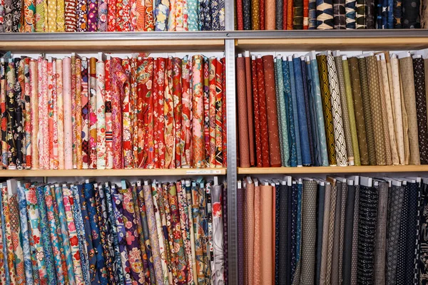 Variety of different fabric bolts exposed on shelves of fabric shop..