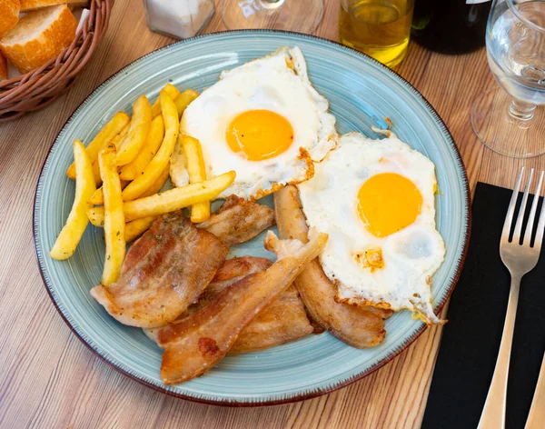 把烤咸肉与炸土豆和鸡蛋一起放在桌子上的蓝色盘子里 — 图库照片