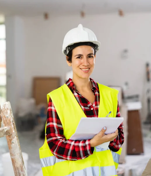 Kvinnlig Ingenjör Byggnadsväst Ler Och Kontrollerar Dokument Reparationsarbeten Inomhus — Stockfoto
