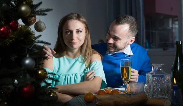 彼女に謝罪笑顔の男を統合 彼女はクリスマスの夜に自宅のテーブルに座っている間 彼女は怒っているふり — ストック写真