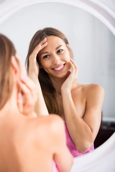 年轻的 面带微笑的西班牙女人对着镜子检查她的脸 — 图库照片