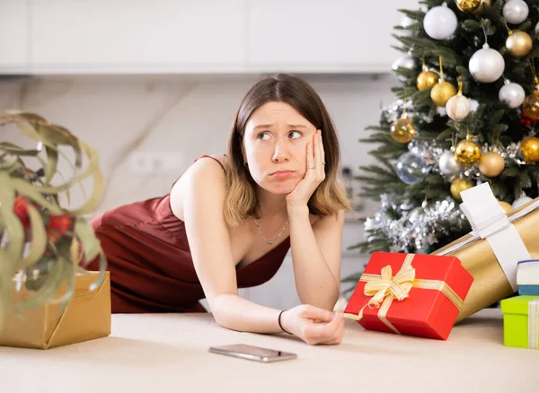 一个悲伤的年轻女人在家里背对着一棵圣诞树和礼物的画像 — 图库照片